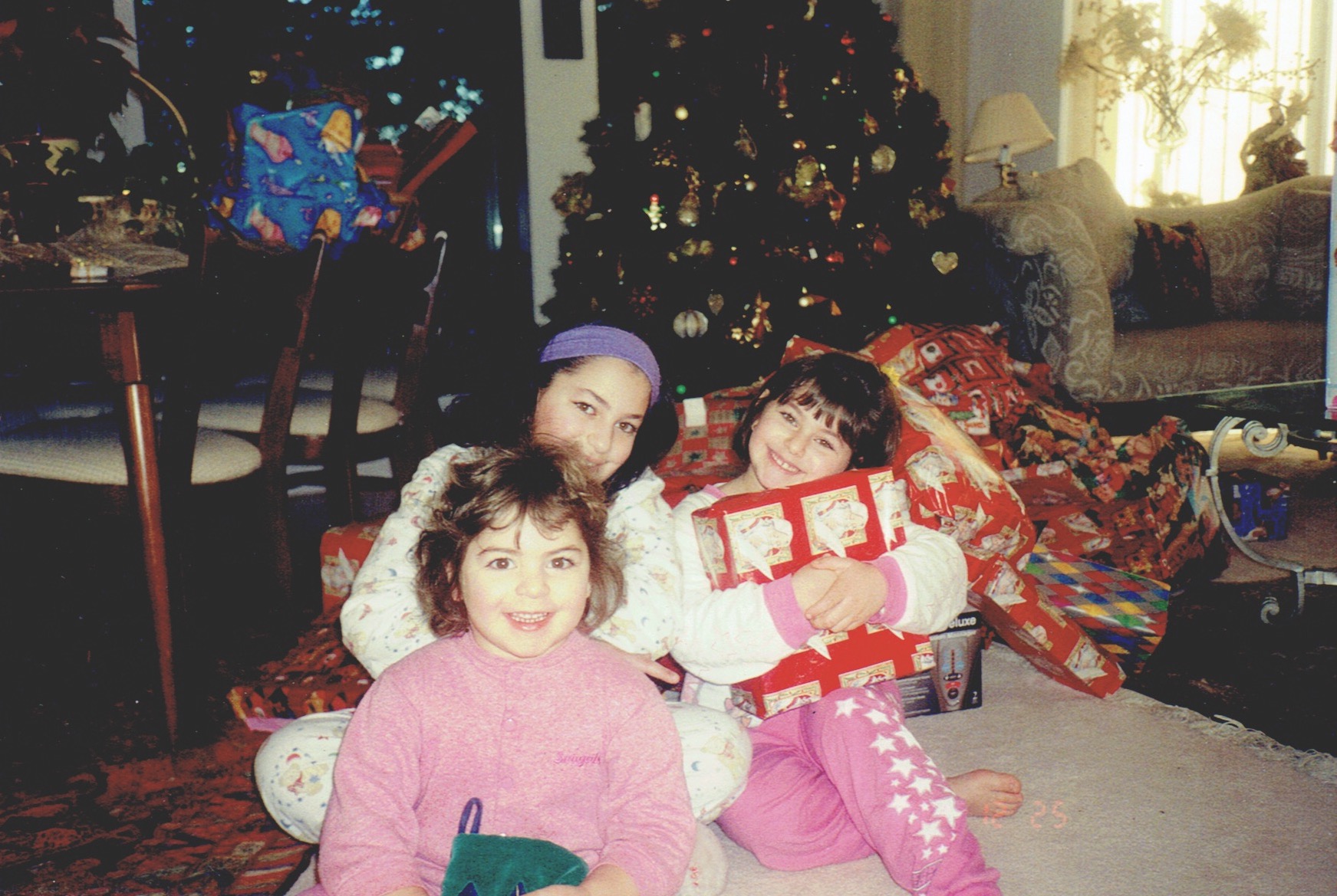 three little girls in front of a Christmas tree with presents
