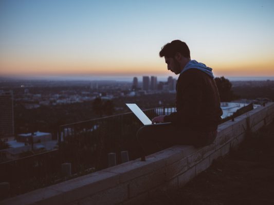 Young man sitting on a ledge with his laptop